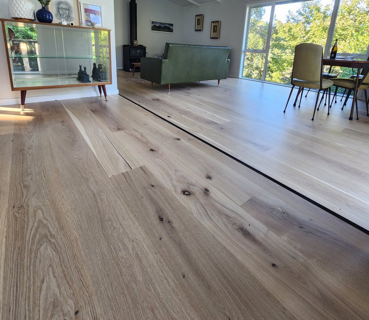 Wide-board timber floor, sanded and finished in a natural matt, in a living room with a window onto the garden